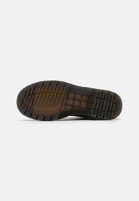 Suela de zapato de goma negra con patrón de agarre texturizado e indentaciones hexagonales. Bordes suaves y ligera translucidez en el centro.