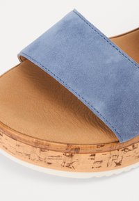 Sandalo con cinturino in suede blu, soletta intermedia simile al sughero e plantare in pelle marrone texturizzata. Presenta una suola in gomma bianca per aderenza e supporto.
