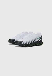 Witte sportschoenen met zwarte accenten, ontworpen met een bovenkant van mesh en een opvallend groen en rood zoolontwerp. Geknoopt met een gevoerde kraag.