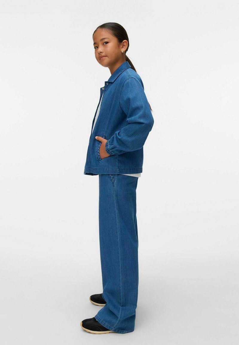 Denim jakna in hlače srednje modre barve, s sproščenim krojem, elastičnimi manšetami na jakni in stranskimi žepi. Črne čevlje s svetlo rjavimi podplati.