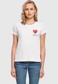 Witte katoenen t-shirt met een rood hart met een ontwerp van de Turkse vlag en het woord "TÜRKİYE" eronder in het grijs. Korte mouwen en ronde hals.
