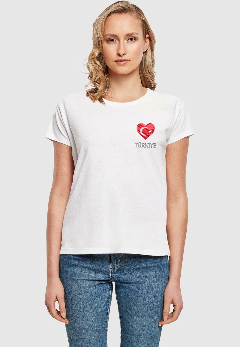 Beyaz pamuklu t-shirt, aşağıda gri renkte "TÜRKİYE" yazısı ile birlikte Türk bayrağı tasarımı olan kırmızı bir kalp şekliyle süslenmiştir. Kısa kollar ve yuvarlak yaka.