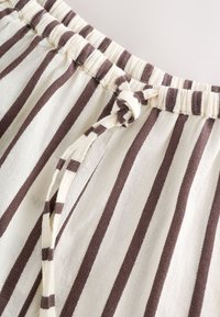 Pantalon en tissu crème avec des rayures verticales marron et une taille élastique avec cordon noué.