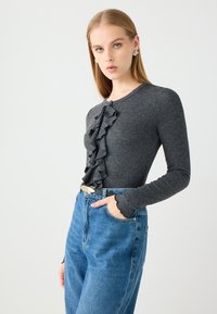 Grijze lange mouw top met een geraffineerd ontwerp aan de voorkant, gecombineerd met hoge taille blauwe denim jeans, met een gegolfde manchette-detail.