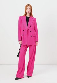 Fuchsia dubbelknopen blazer met bijpassende brede broekspijpen. Gladde stof met gestructureerde schouders, zwarte accenten en voorzakken.