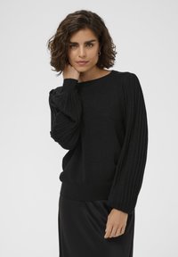 Sort pullover sweater lavet af blødt, struktureret materiale. Har ribbede puffærmer og en klassisk rund halsudskæring. Glat, afslappet pasform.