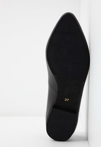 Semelle d'une chaussure de ville noire pointue avec grip texturé et numéro de taille 37 en impression dorée sur fond blanc.