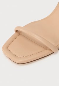 Sandale en cuir beige avec un design à bout carré, une seule sangle sur le pied et des détails de couture subtils le long du bord.