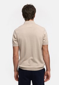 Beige kortermet polo skjorte med ribbestrikket krage og mansjetter, tettsittende fasong, myk tekstur og rett skjortekant. Ingen synlig logo.