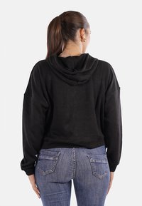 Felpa nera con cappuccio, dal fit rilassato e spalle scese, abbinata a jeans blu aderenti con tasche posteriori.