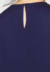 Marinblått tyg med en nyckelhålsöppning på baksidan. Texturen är slät och designen har en enkel, odekorerad skärning.