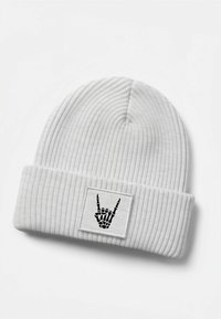White ribbed knit beanie featuring a black patch with a skeleton hand making a "rock on" gesture.