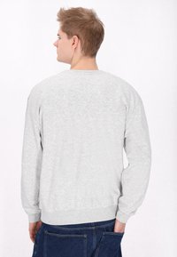 Maglione grigio con collo rotondo, polsini e orlo a coste, realizzato in un morbido tessuto testurizzato, mostrato da dietro su uno sfondo neutro.