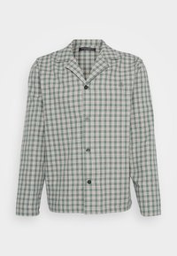 Chaqueta de camisa a cuadros verde y blanca con solapas reversibles, mangas largas y botones negros, que presenta un sutil logo en el pecho.