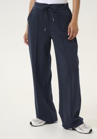 Marineblauwe sportbroek met een trekkoord in de taille, wijde benen en zijzakken. Gemaakt van een gestructureerde stof, geschikt voor casual gebruik.