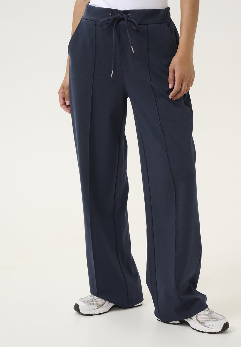 Marineblauwe sportbroek met een trekkoord in de taille, wijde benen en zijzakken. Gemaakt van een gestructureerde stof, geschikt voor casual gebruik.