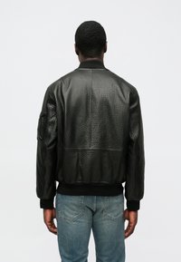 Mustast nahast pommitusjakk tekstuurse viimistlusega, soonikkoes varrukaotsade ja äärega, tagaosa õmblus ning tööriistatasku vasakul varrukal.