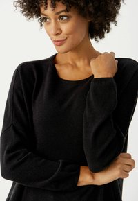 Schwarzer Strickpullover mit rundem Ausschnitt, langen Ärmeln und lockerer Passform. Der Stoff wirkt weich und verfügt über texturierte Details.
