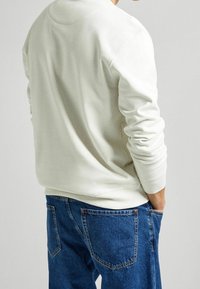 Felpa bianca con polsini e orlo a coste, abbinata a jeans in denim blu con una texture sbiadita e tasche posteriori.