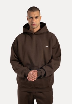 Braun Kapuzenpullover aus weichem Stoff, mit einer Fronttasche und gerippten Bündchen. Kleines Logo-Akzent auf der Brust. Lockere Passform.