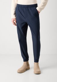 Marineblauwe, lichtgewicht broek met een elastische tailleband, zijzakken en taps toelopende boorden, gecombineerd met beige enkellaarsjes.