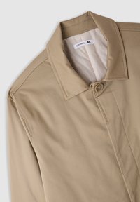 Giacca beige con un colletto strutturato, chiusura a un bottone e texture liscia. Etichetta con la scritta "Terranova XL". Decorazioni cucite sulle cuciture.