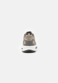 Sneakers leggeri beige con una tomaia in rete, dettagli grigi e una robusta suola bianca; dotati di un colletto imbottito e un'etichetta sul tallone.