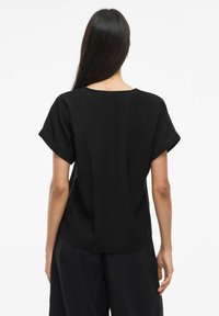 Top nero a maniche corte con una silhouette ampia, scollatura rotonda e orli arrotolati, realizzato in tessuto morbido. Design semplice, senza motivi o dettagli visibili.