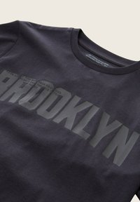 Mörkgrå t-shirt med rund halsringning och stor texten "BROOKLYN" tryckt över bröstet i en något mörkare nyans.