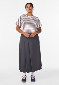 Triibuline lühikeste varrukatega särk roosa ja tumepunase toonides, koos plisseeritud pahkluuni ulatuva halli seelikuga. Jalatsiteks on tumesinised vabaajajalatsid roosade paeltega.