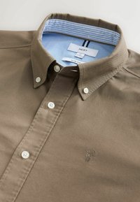 Cămașă maro slim-fit cu guler cu buton, având butoane albe, guler interior cu dungi bleu deschis și un detaliu subtil brodat cu logo.