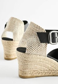 Sandales compensées en espadrilles tissées avec tissu à carreaux beige, brides de cheville noires, boucles argentées et semelles plateforme en jute tressé.