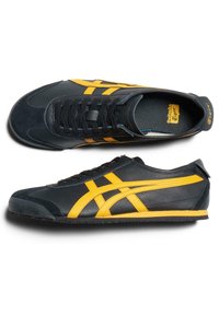 Svarta träningsskor i läder, med gula accenter och ränder, rund tå, strukturerad yta och platt gummisula.