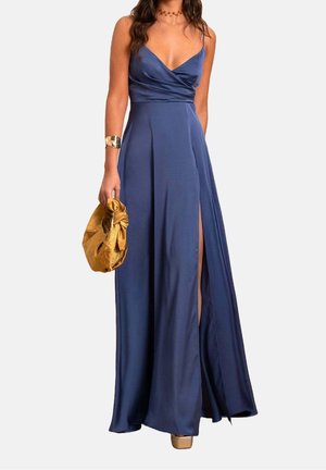 Femme portant une robe bleu marine sans manches avec une fente haute sur la cuisse, tenant un sac à main doré et portant un bracelet et un collier dorés.