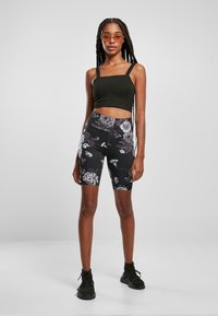 Svart crop top med firkantet utringning, sammen med svarte sykkelshorts med blomstermønster. Modellen har på seg svarte sneakers og tonede oransje solbriller.