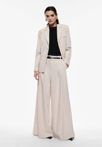 Abito a righe crema con pantaloni larghi e blazer su misura, abbinato a un top nero a coste e una cintura nera. Texture liscia.