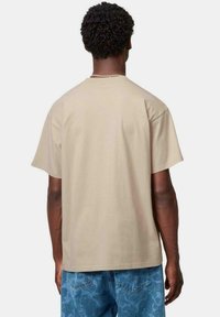Camiseta de manga corta beige en un corte relajado, hecha de algodón suave, con cuello redondo y detalles cosidos a lo largo de los hombros.