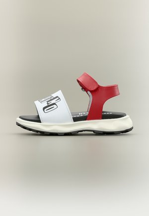 Crvena i bijela sandala s podesivim remenom, crnim potplatom i velikim crnim tekstom na prednjem remenu.