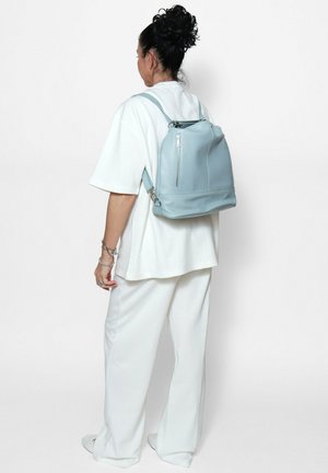 Zaino di pelle azzurro chiaro con due spallacci regolabili, una maniglia superiore e una tasca frontale con zip. Texture liscia e forma strutturata.