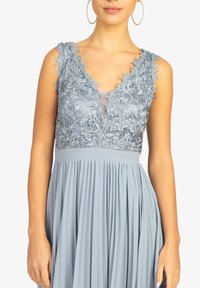 Robe bleu clair avec un décolleté en V profond, des détails en dentelle délicate aux épaules, et une jupe plissée, fabriquée en tissu doux.
