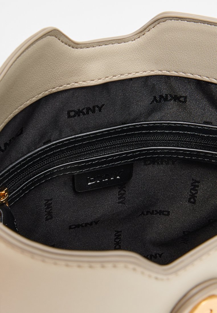 Beiger Lederhandtascheninnenraum mit schwarzem Stofffutter, das mit dem wiederholten "DKNY"-Logo versehen ist. Enthält eine Reißverschlusstasche und glatte Kanten.