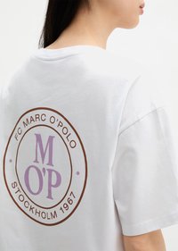 Άτομο που φοράει λευκό T-shirt με κυκλικό λογότυπο στην πλάτη που γράφει "FC Marc O'Polo Stockholm 1967" και μεγάλα γράμματα "M O'P" σε μωβ χρώμα.