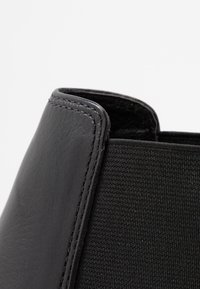 Botín de tobillo de cuero negro y tejido, con un exterior de cuero suave y un panel de tejido texturizado, y con costuras en contraste a lo largo de los bordes.