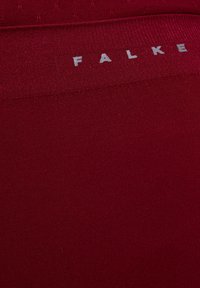 Czerwona jednolita tkanina o gładkiej fakturze. W górnej części wyraźnie widoczne jest jasnoszare logo "FALKE".