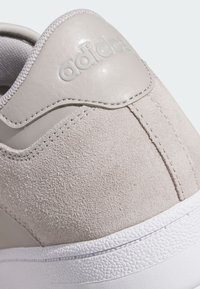 Baskets gris clair présentant une combinaison de textures lisses et en daim, avec un détail cousu et une semelle en caoutchouc blanc. Logo de la marque embossé sur le talon.