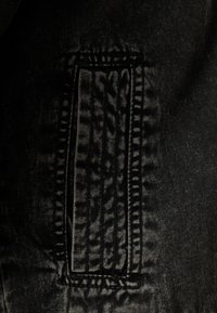 Svart denimtyg med en rektangulär, stickad fickkontur med texturerade detaljer och skuggeffekter.