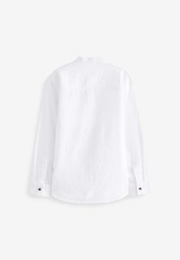 Chemise blanche à manches longues avec poignets boutonnés, couture visible sur le haut du dos, présentée à plat face vers le bas sur un fond uni.