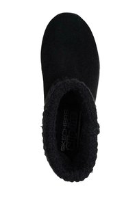 Zapato negro tipo slip-on con parte superior suave y texturizada, forro mullido y punta redondeada. Cuenta con logotipo en la plantilla y suela exterior flexible.