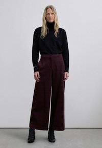 Suéter negro de cuello alto combinado con pantalones de cuadros burdeos de pierna ancha y botas negras con tacón. Parte superior ajustada, pantalones fluidos con un patrón de cuadros.