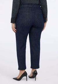 Mörkblå jeans i denim med rynkad midjeresår, smal passform och raka ben. Kombinerade med svarta spetsiga klackskor för kontrast.